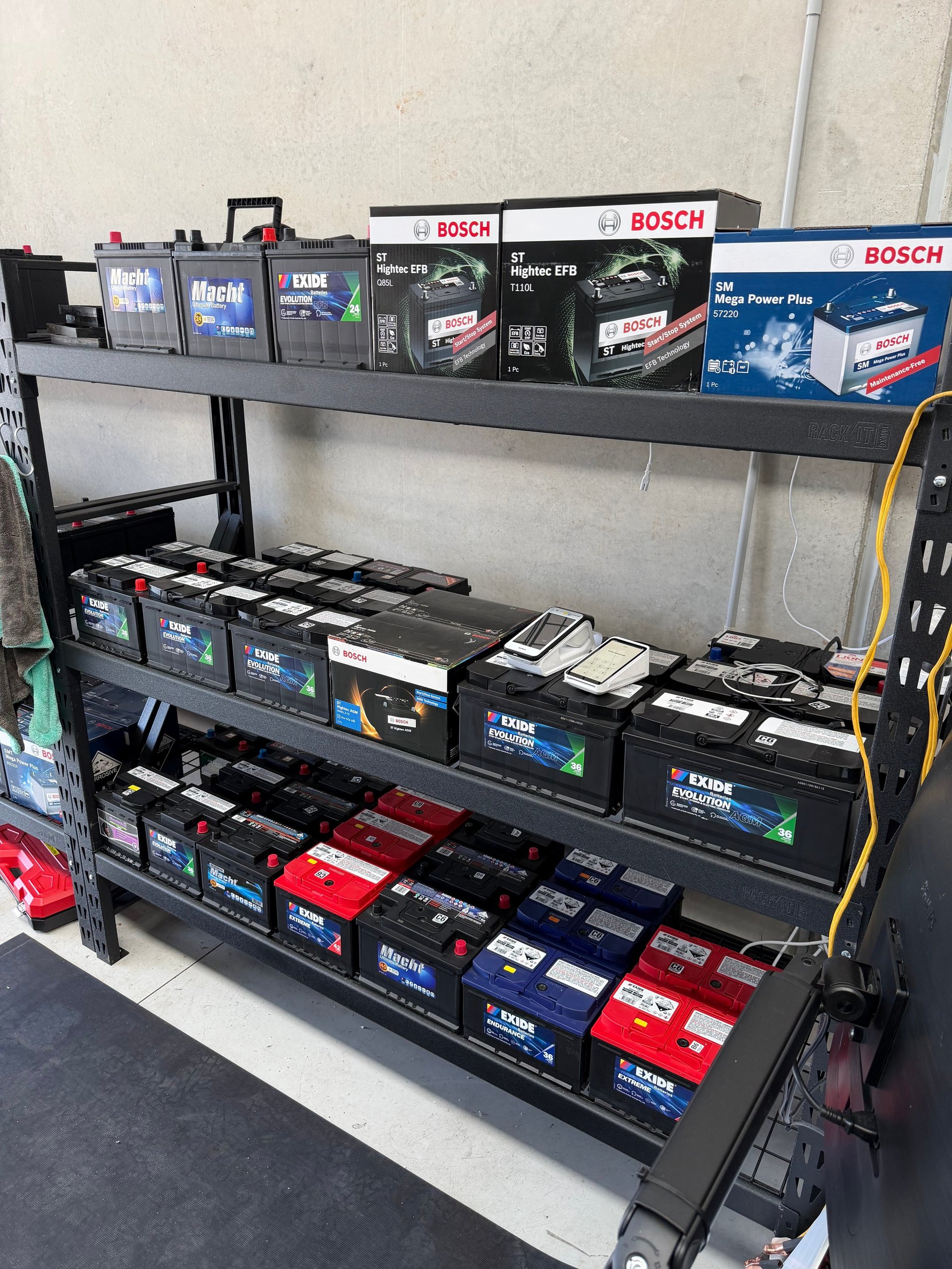Three-tiered metal shelf display stocked with various Bosch car batteries and automotive products