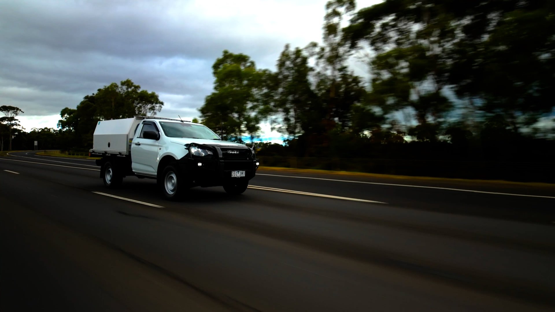 White utility van driving on a highway with motion blur, trees and cloudy sky in the background